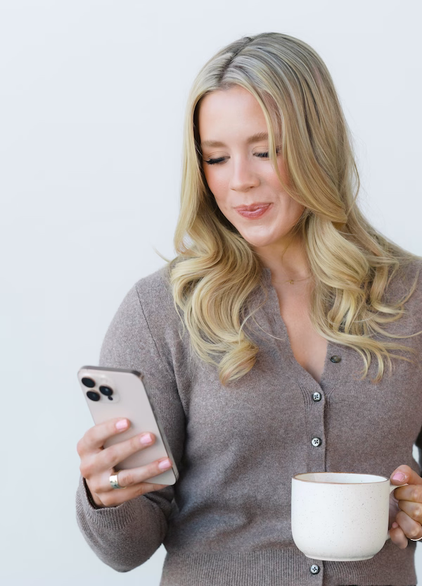 Savannah Abney looking at her smartphone while holding a coffee mug, representing the modern, everyday expectation for founder digital presence.